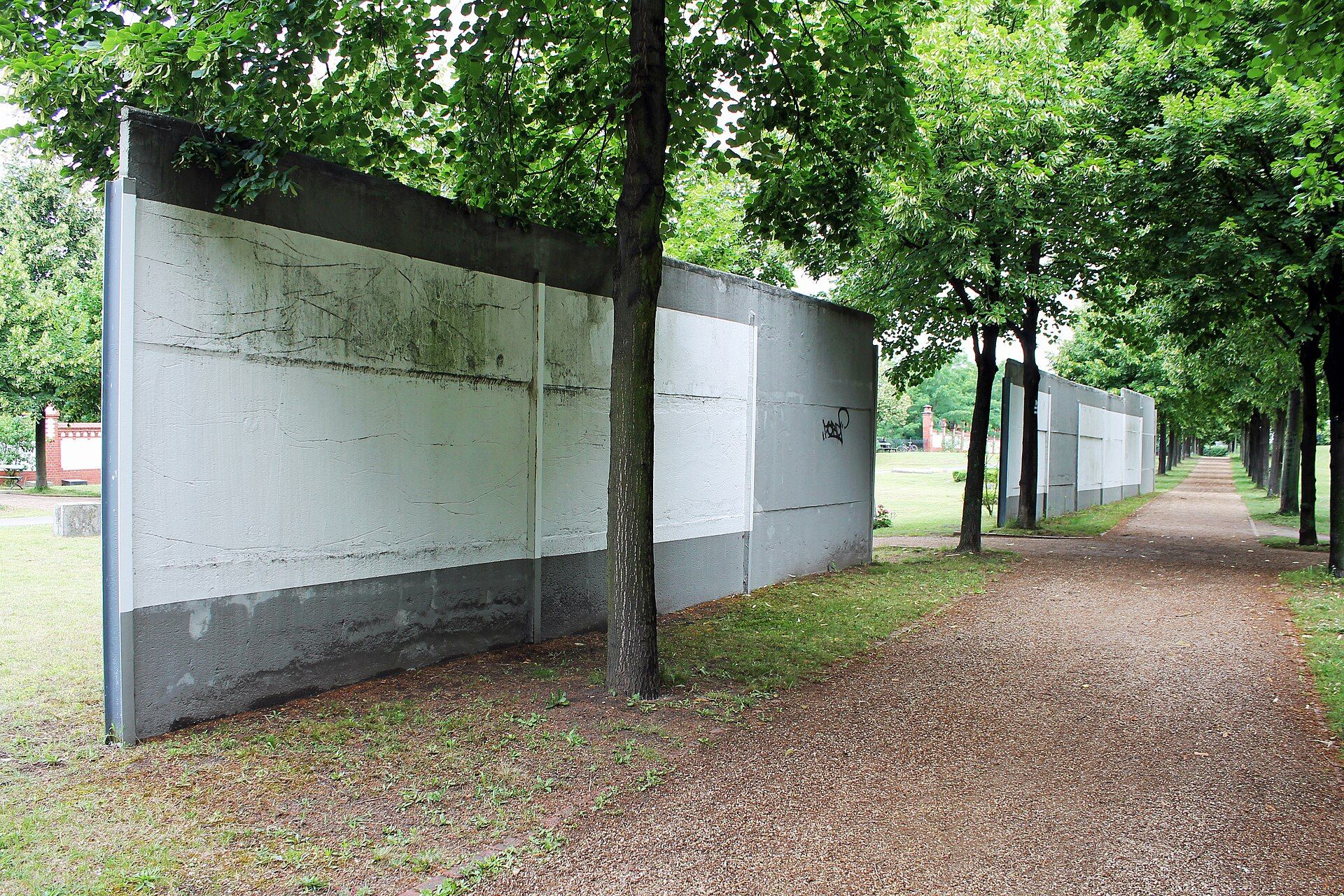Erhaltene weiß-graue Hinterlandmauer zwischen Bäumen im Invalidenfriedhof