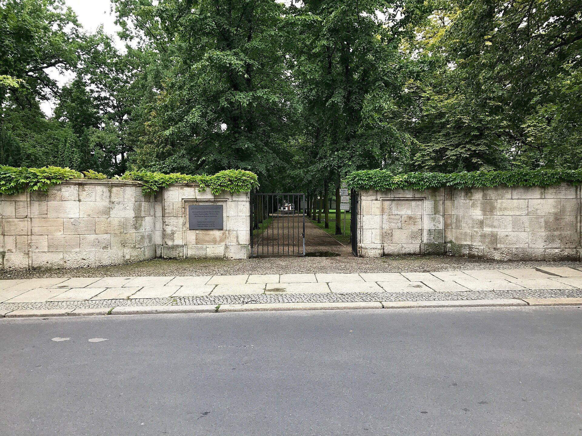 Mit Efeu bewachsene Friedhofsmauer und offenes Metalltor des Invalidenfriedhofs an der Scharnhorststraße